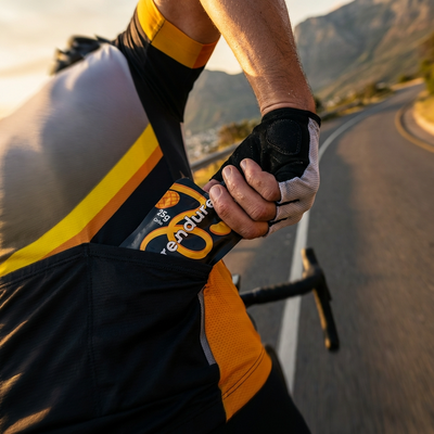 Person riding a bicycle on a road with mountains in the background while reaching to their back pocket to get the Purendure pouch