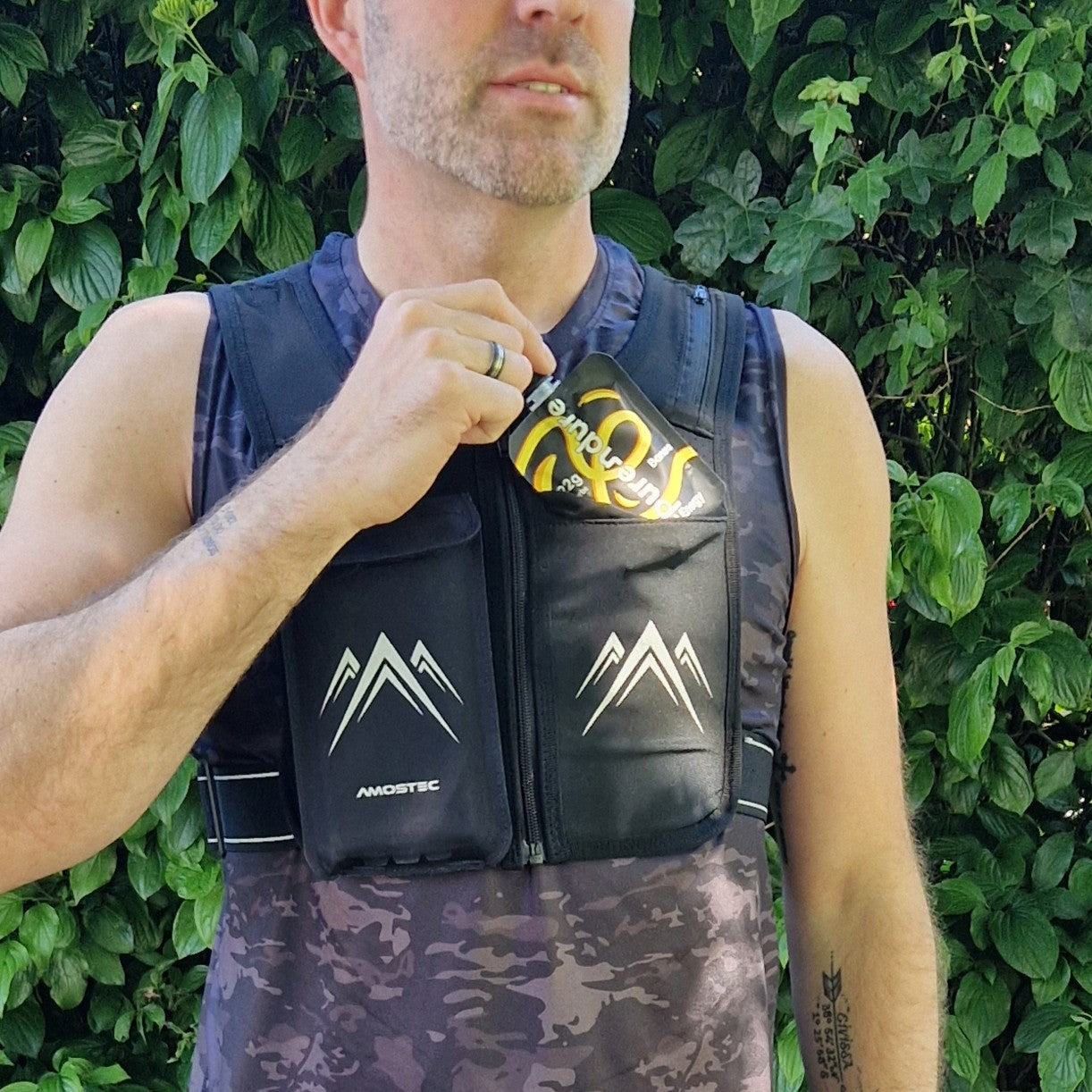 Person wearing a black life vest with mountain logos against a green leafy background.